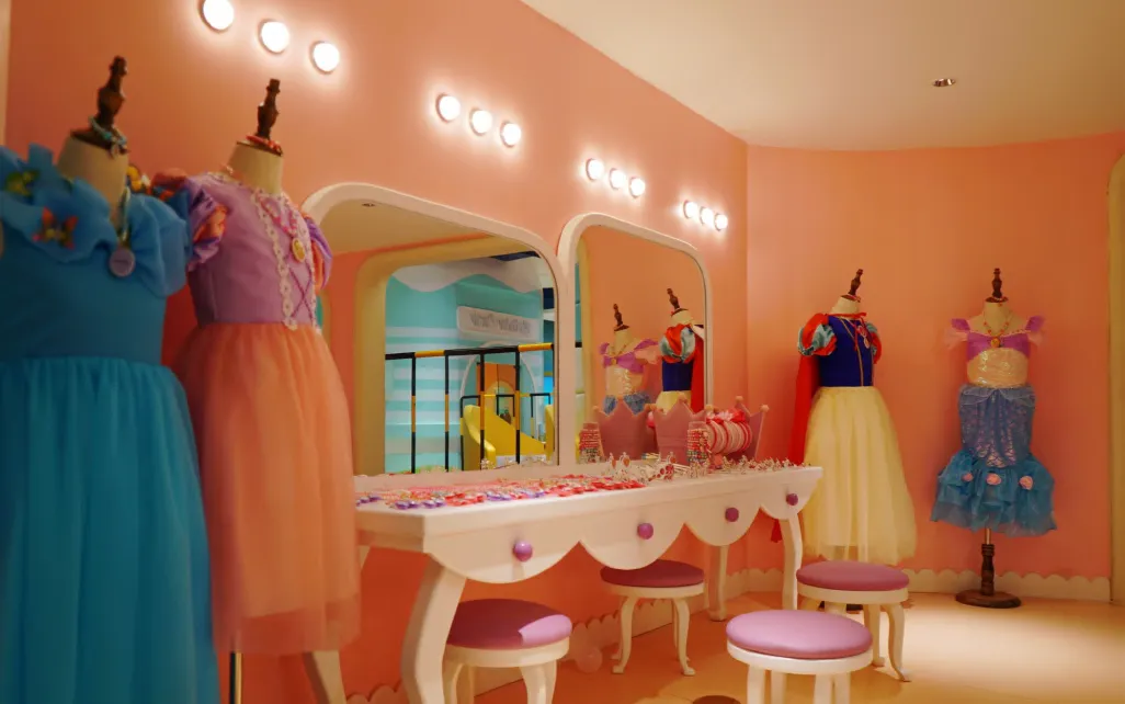 ركن لعب بتصميم غرفة تبديل أزياء داخل صالة ألعاب، يضم فساتين أميرات ملونة على مجسمات عرض وطاولة مكياج بمرايا مضيئة