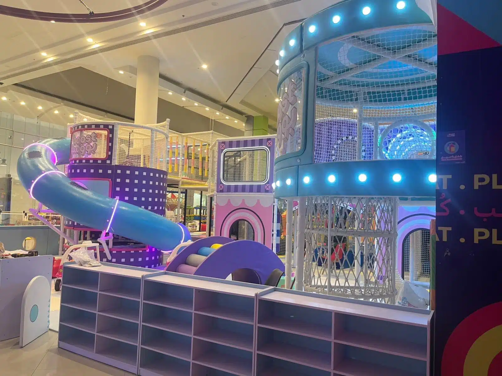 هيكل ألعاب داخلي ملون داخل مركز يضم زحليقة أنبوبية زرقاء متعددة المستويات وأبراج شبكية مضيئة مع مناطق تسلق وممرات آمنة