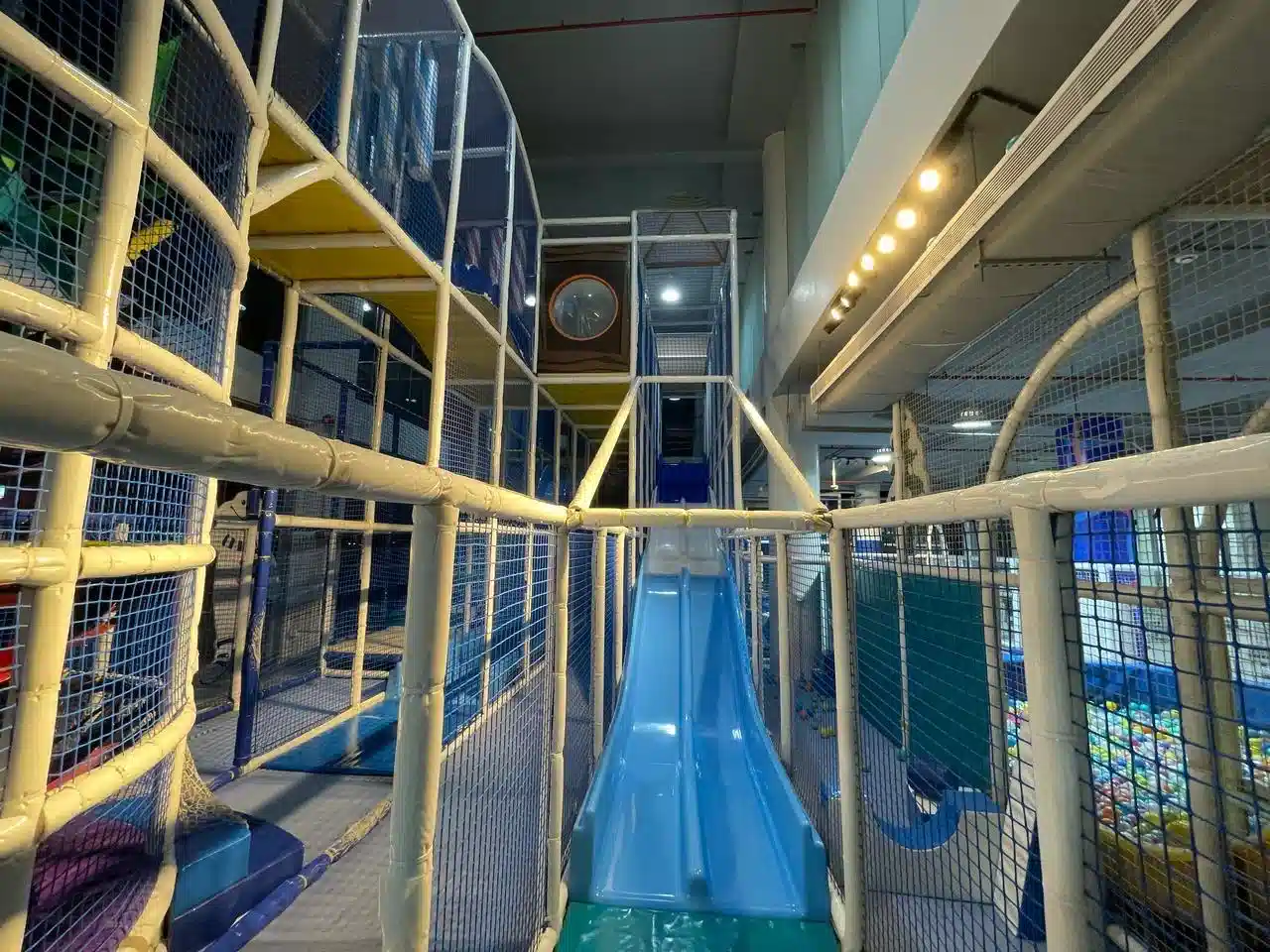هيكل ألعاب متعدد المستويات داخل صالة يضم زحليقة زرقاء طويلة وممرات شبكية محاطة بإطارات معدنية آمنة مع مناطق تسلق