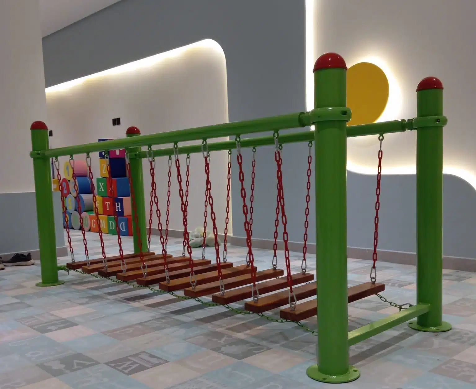 جسر توازن معلق بسلاسل معدنية وألواح خشبية داخل صالة ألعاب مخصصة لتجهيز الروضات مع أرضية آمنة